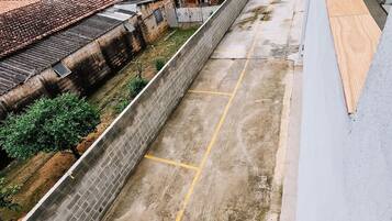 A rooftop with a concrete barrier, a paved area with yellow lines, and a view of buildings with red-tiled roofs.