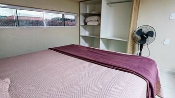 Ein Schlafzimmer mit einem Bett, einem Fenster, einem Ventilator und einem Regal.
