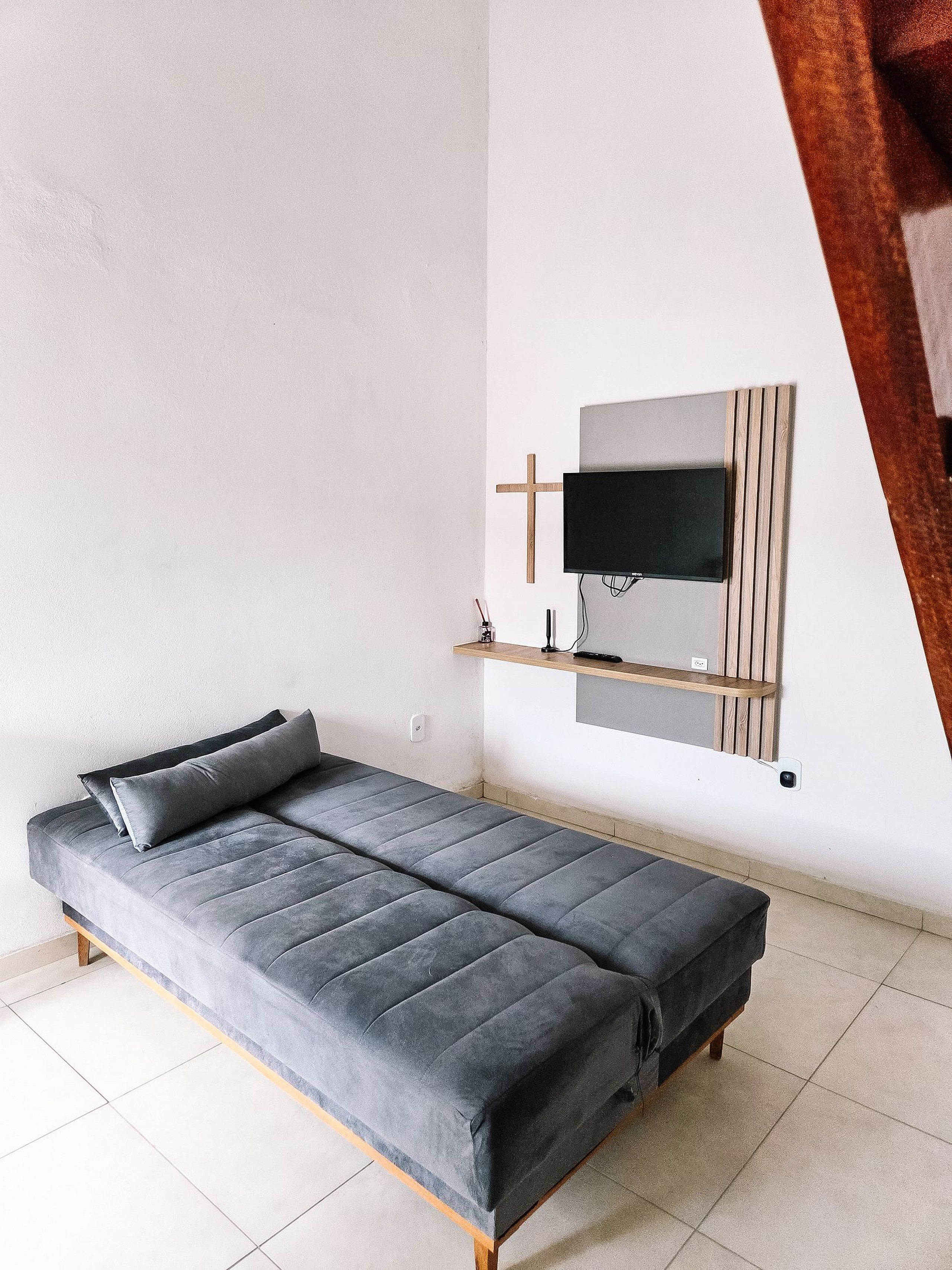 A modern room with a grey sofa, a mounted TV, and a wooden shelf.