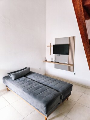 A modern room with a grey sofa, a mounted TV, and a wooden shelf.