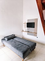 Una habitación moderna con un sofá gris, un televisor montado y un estante de madera.