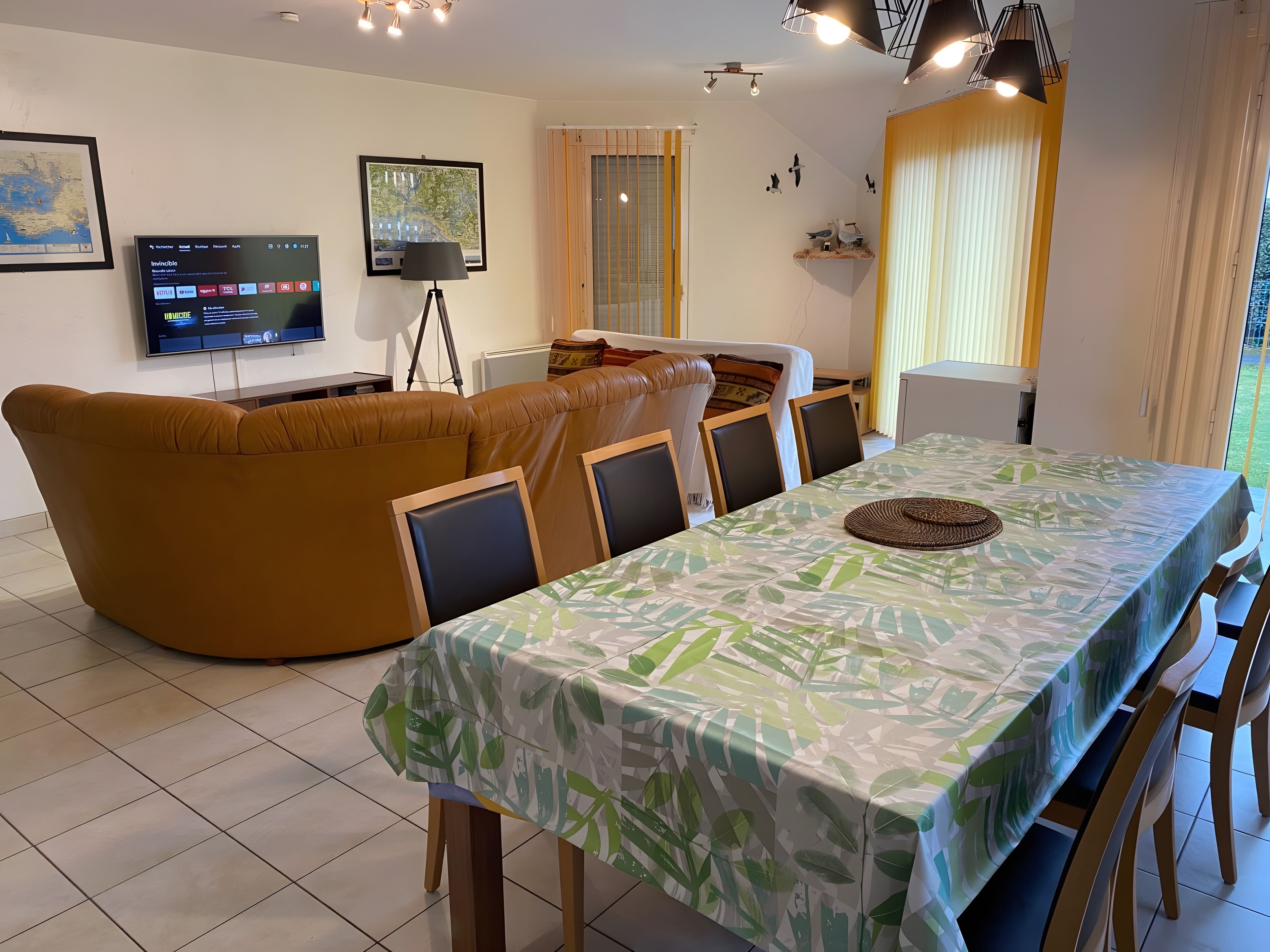 A modern living room with a sofa, a dining table with chairs, a TV, and a window with curtains.