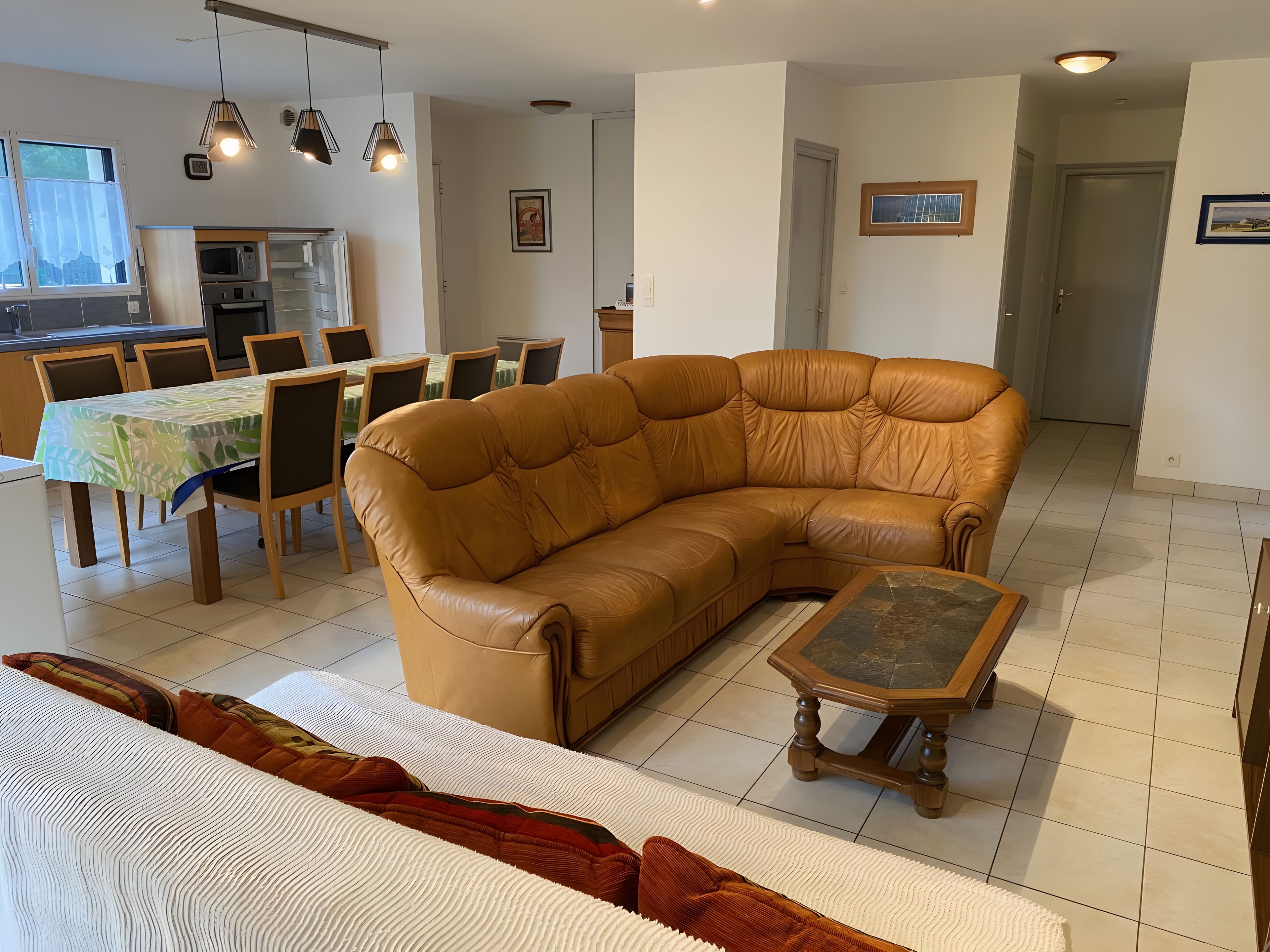 A living room with a sectional sofa, a dining table with chairs, a kitchen area, and a hallway.