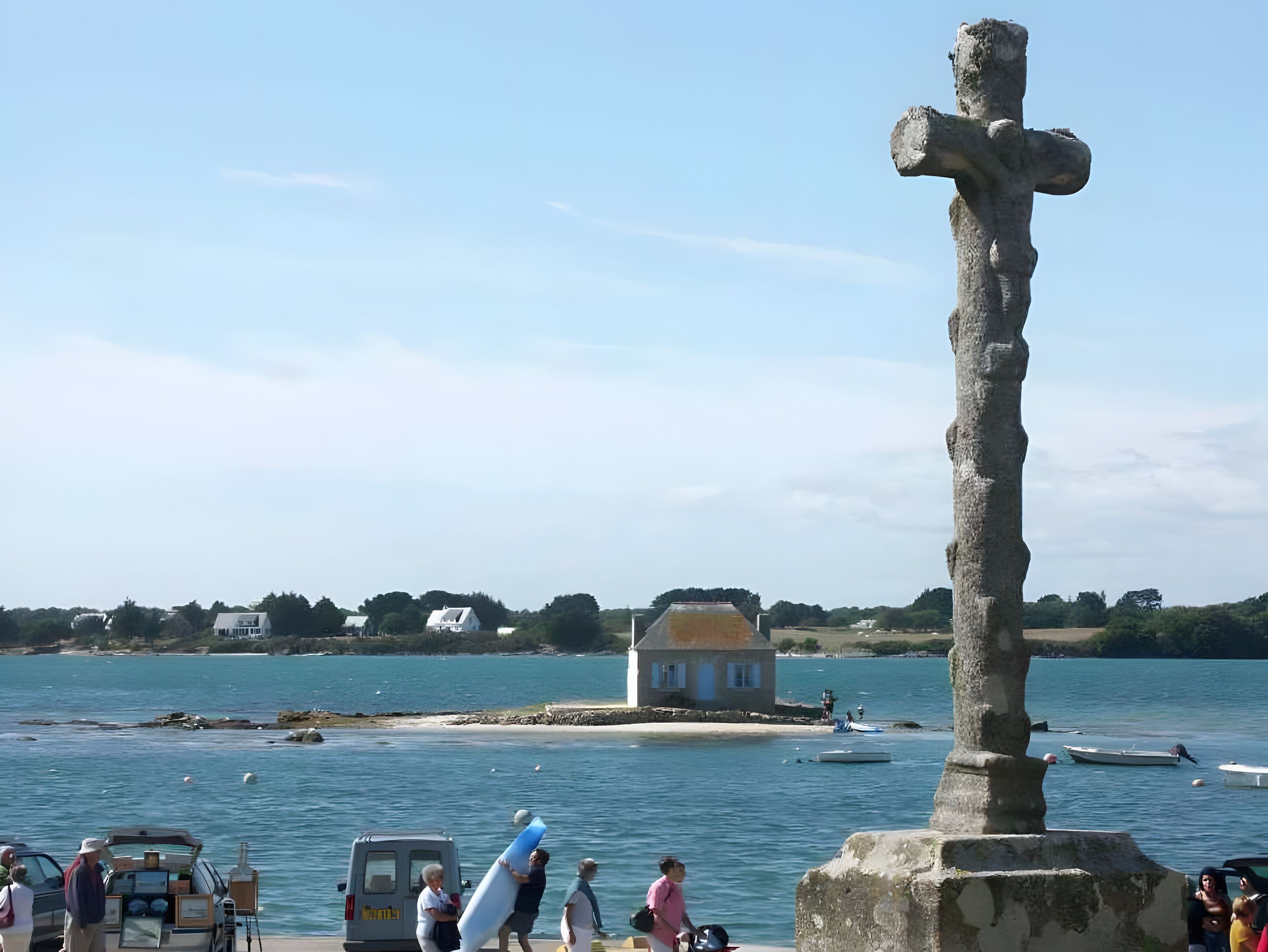 A coastal scene with a stone cross, a small house, and boats on the water.