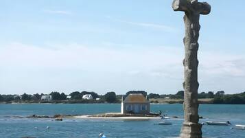 A coastal scene with a stone cross, a small house, and boats on the water.