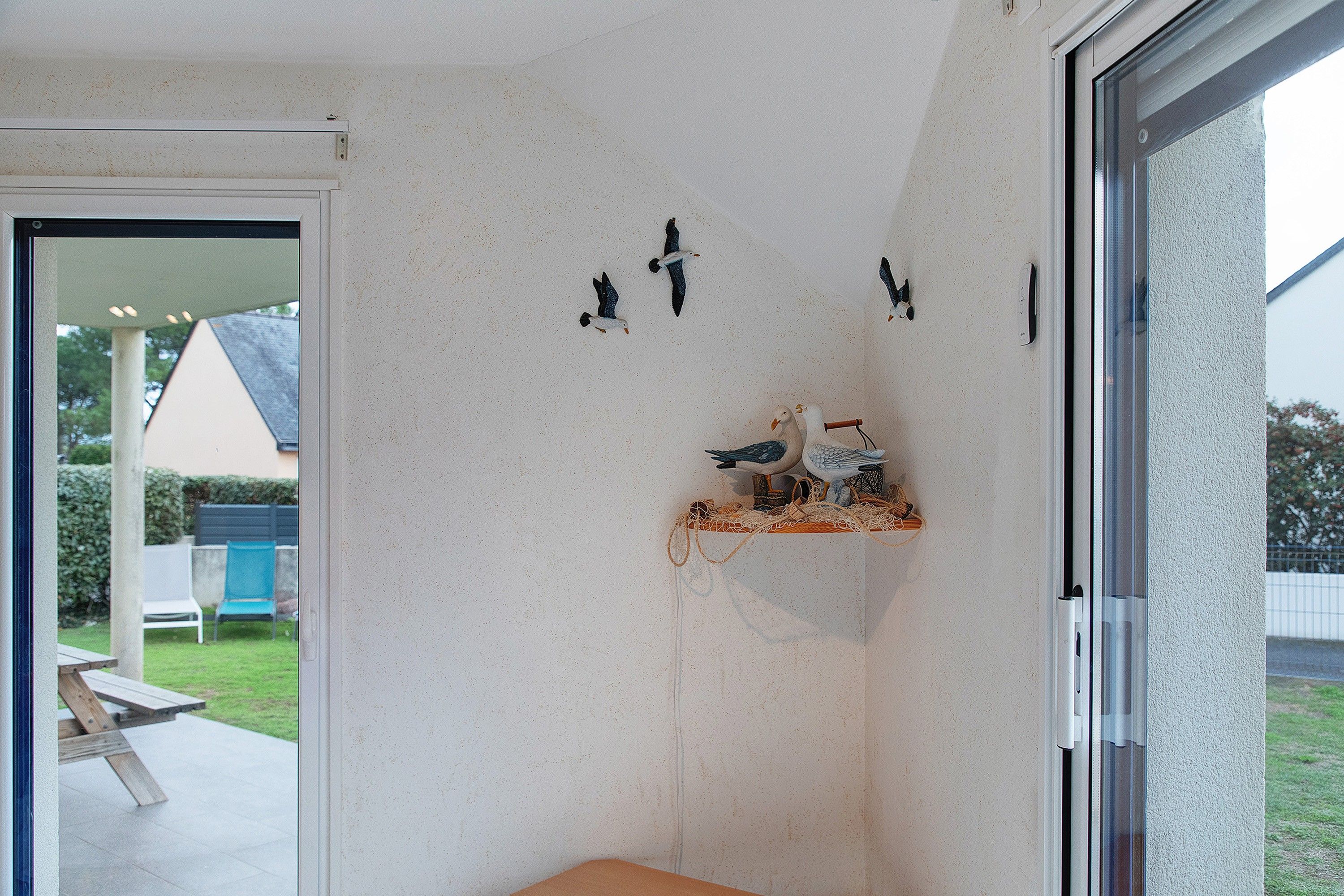 A room with a glass door leading to an outdoor area, a small table, and a shelf with decorative items.