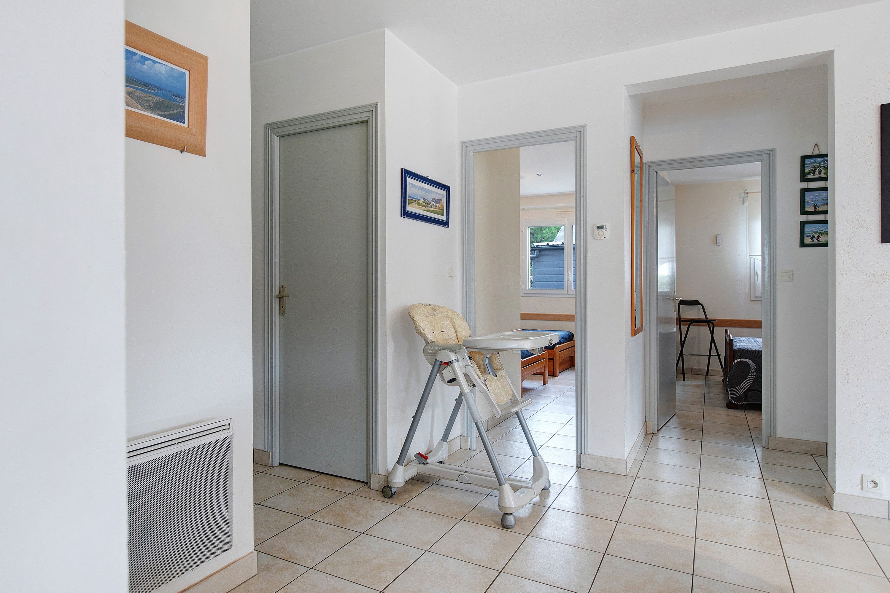 A hallway with a baby walker, a door, and a view into another room with a bed and a chair.