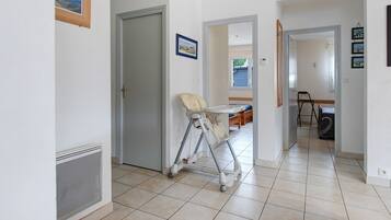 A hallway with a baby walker, a door, and a view into another room with a bed and a chair.