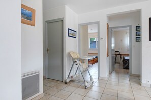 Un pasillo con un andador para bebé, una puerta y vistas a otra habitación con una cama y una silla.