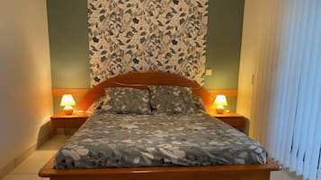 A bed with a leaf-patterned bedspread, two bedside lamps, and a wall with a floral wallpaper.