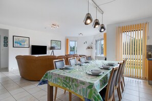 Un comedor con una mesa dispuesta para cuatro personas, un sofá de cuero marrón y un televisor en la pared.