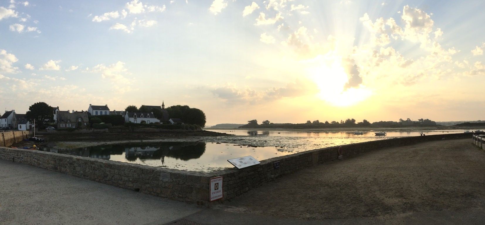 Une vue sur le front de mer, avec un mur de pierre, un panneau et des bâtiments en arrière-plan.