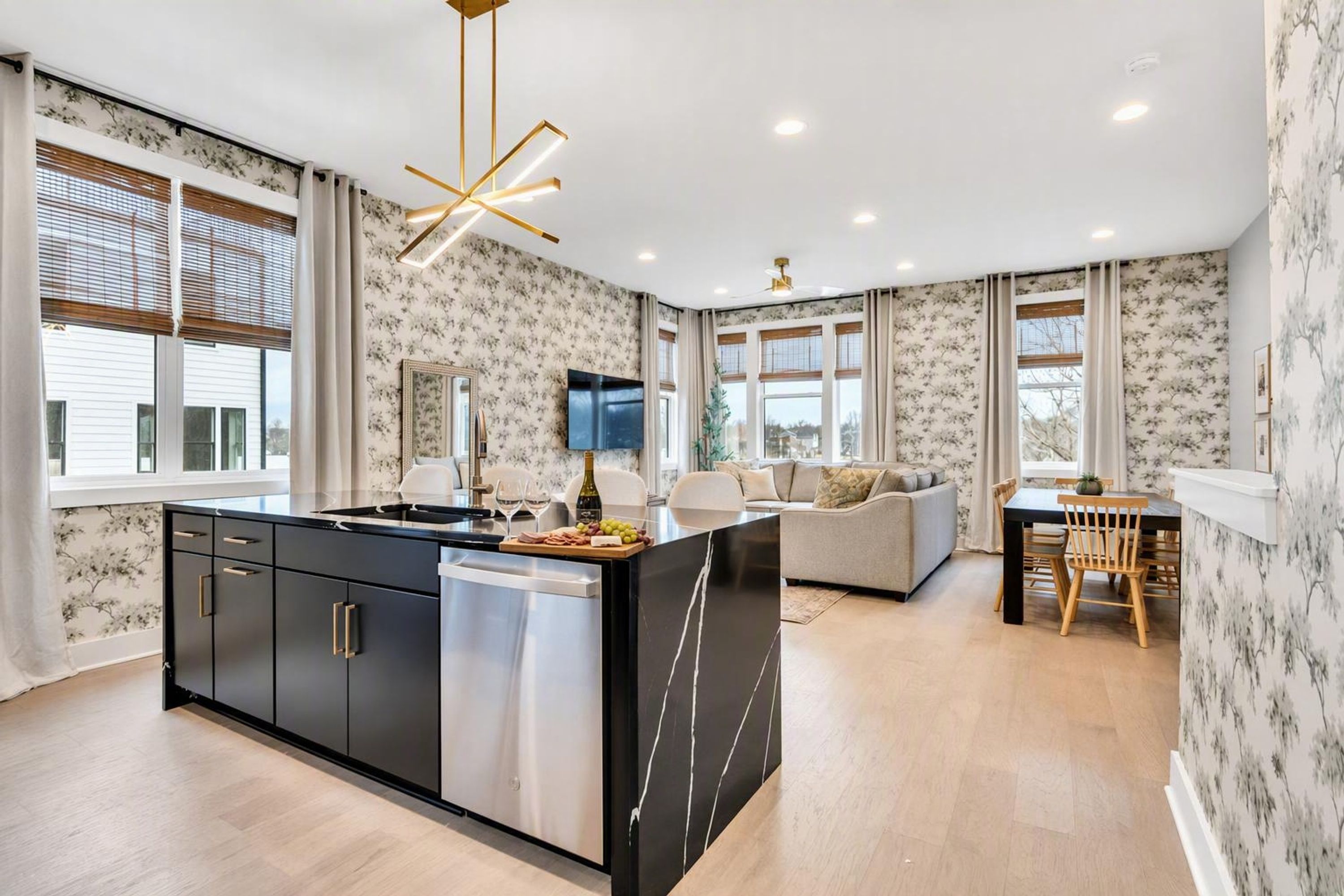 A modern kitchen with a central island, a dining area with a wooden table and chairs, and a living area with a sofa and a flat-screen TV.