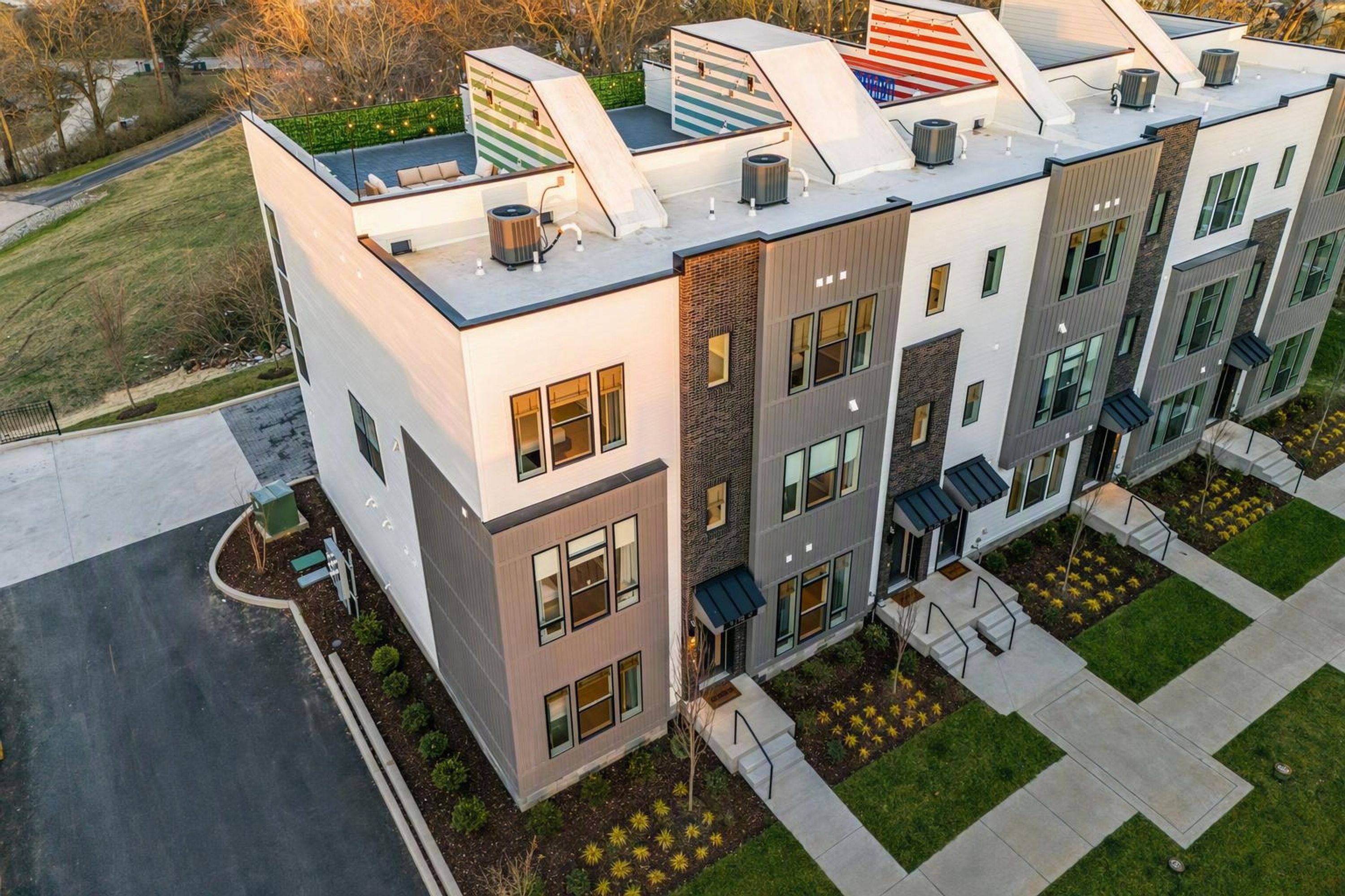 A multi-story residential building with a flat roof, large windows, and a landscaped front yard.