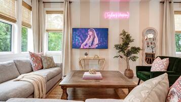 A living room with a television mounted on the wall, a wooden coffee table, a green sofa, and a beige couch.