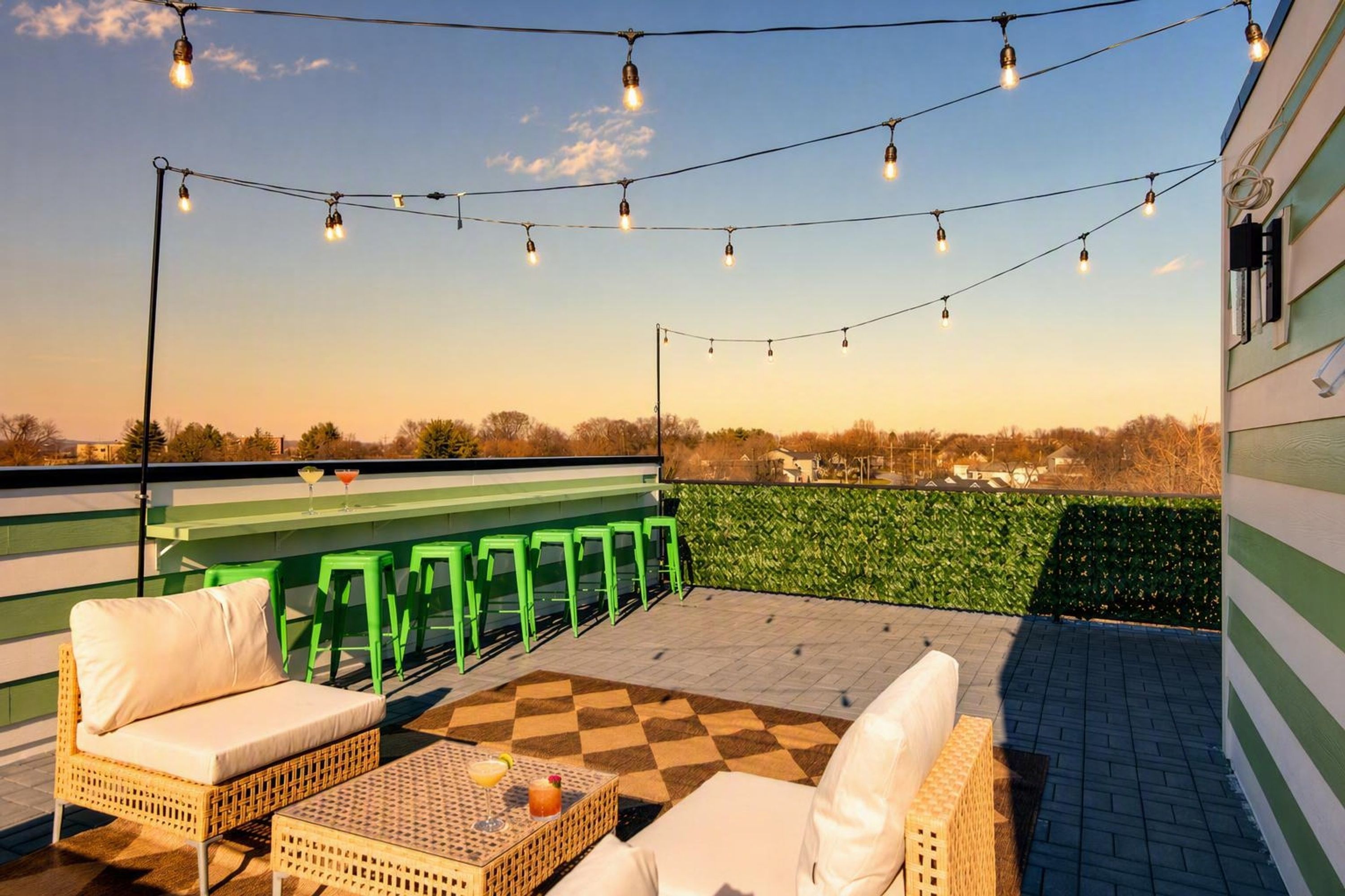 Une terrasse extérieure agrémentée de guirlandes lumineuses, de chaises vertes et d’un sol à carreaux.