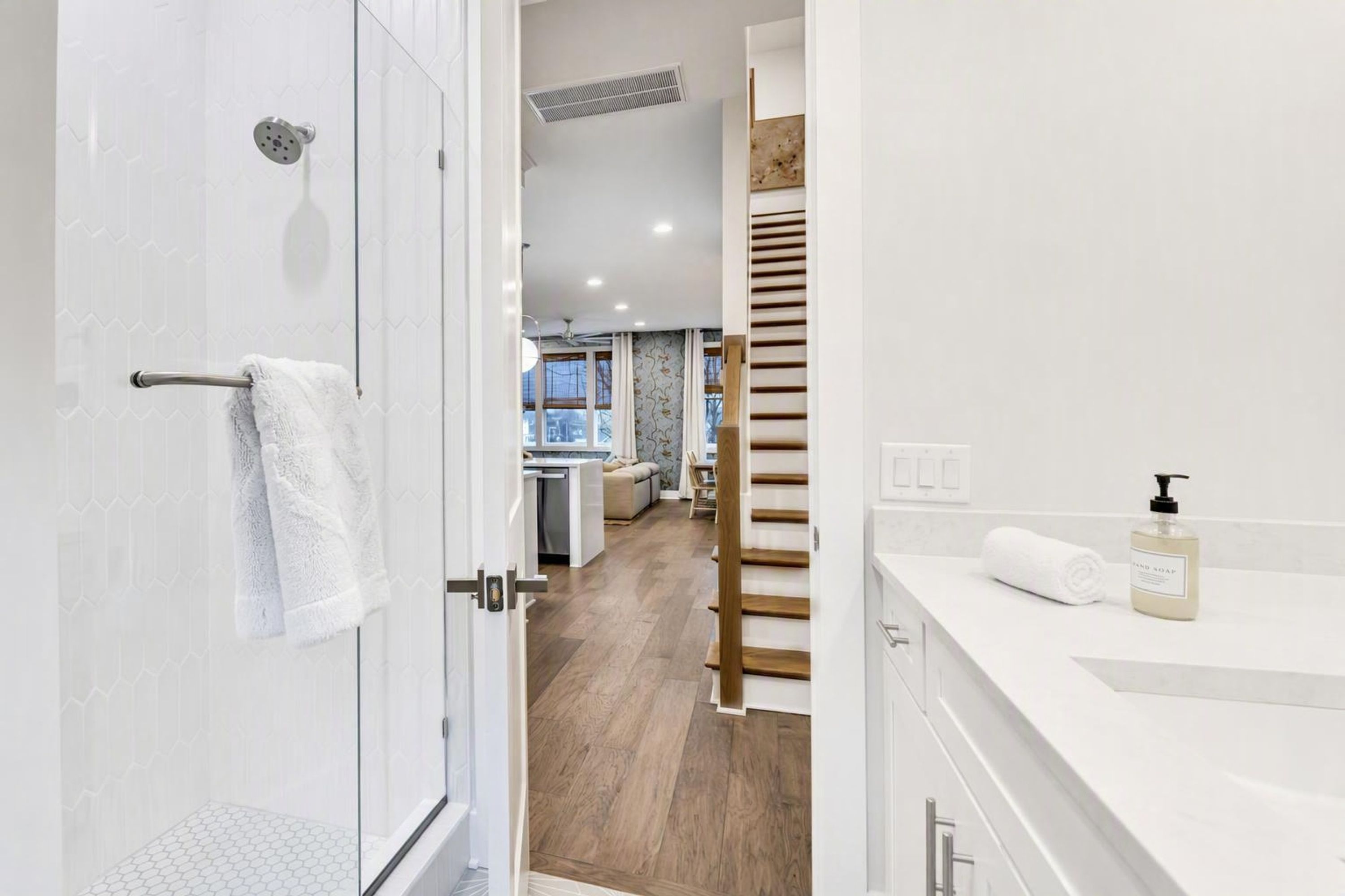 A modern bathroom with a shower, a towel rack, and a sink with a soap dispenser.