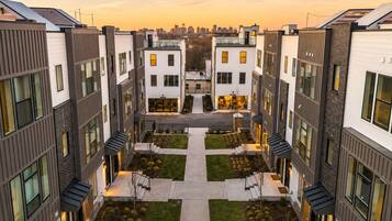 A modern apartment complex with a central courtyard, multiple balconies, and a city skyline in the background.
