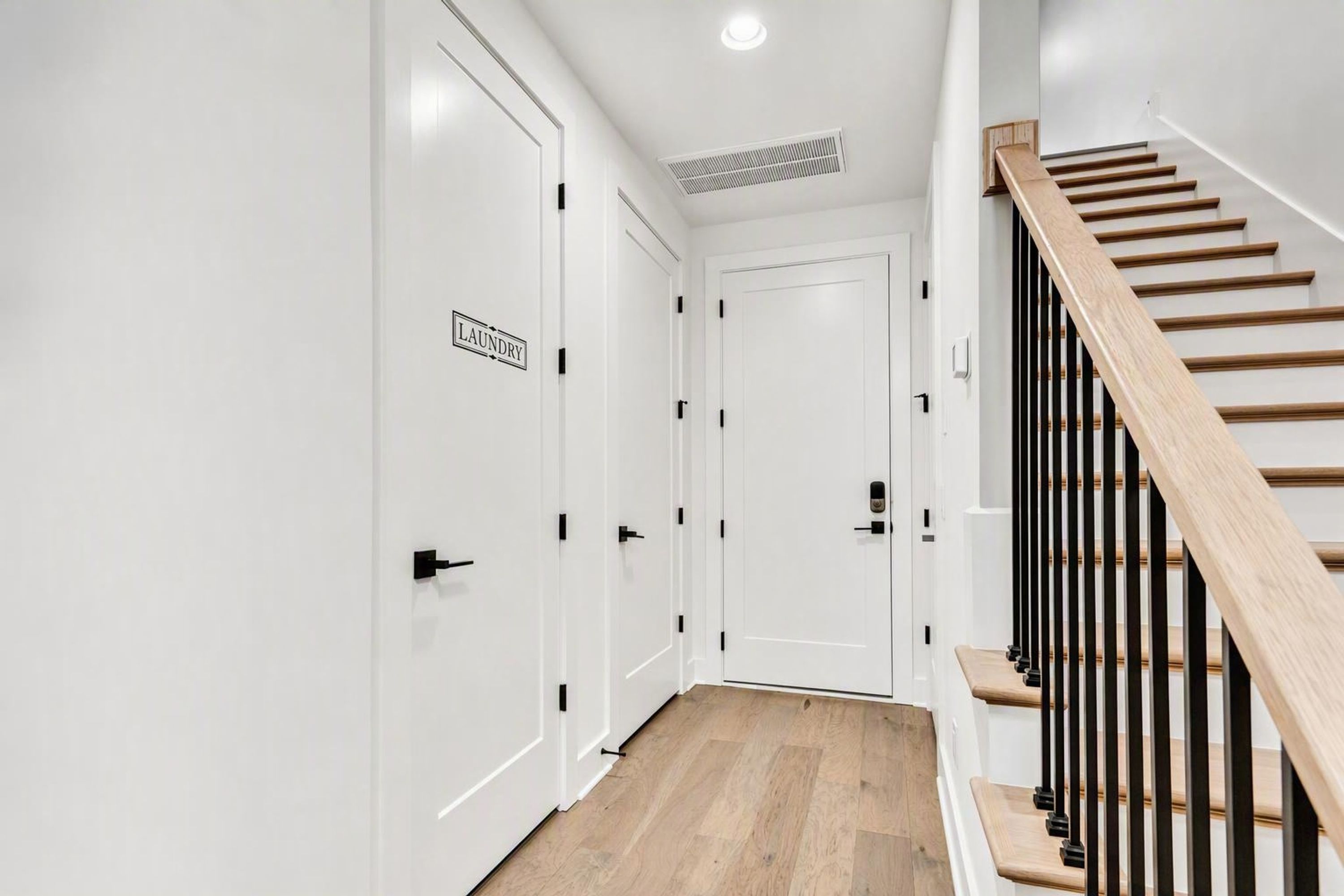 Un couloir avec des portes blanches, dont une porte sur laquelle est inscrit « LINGERIE », qui mène à un escalier avec des marches en bois et des rampes noires.