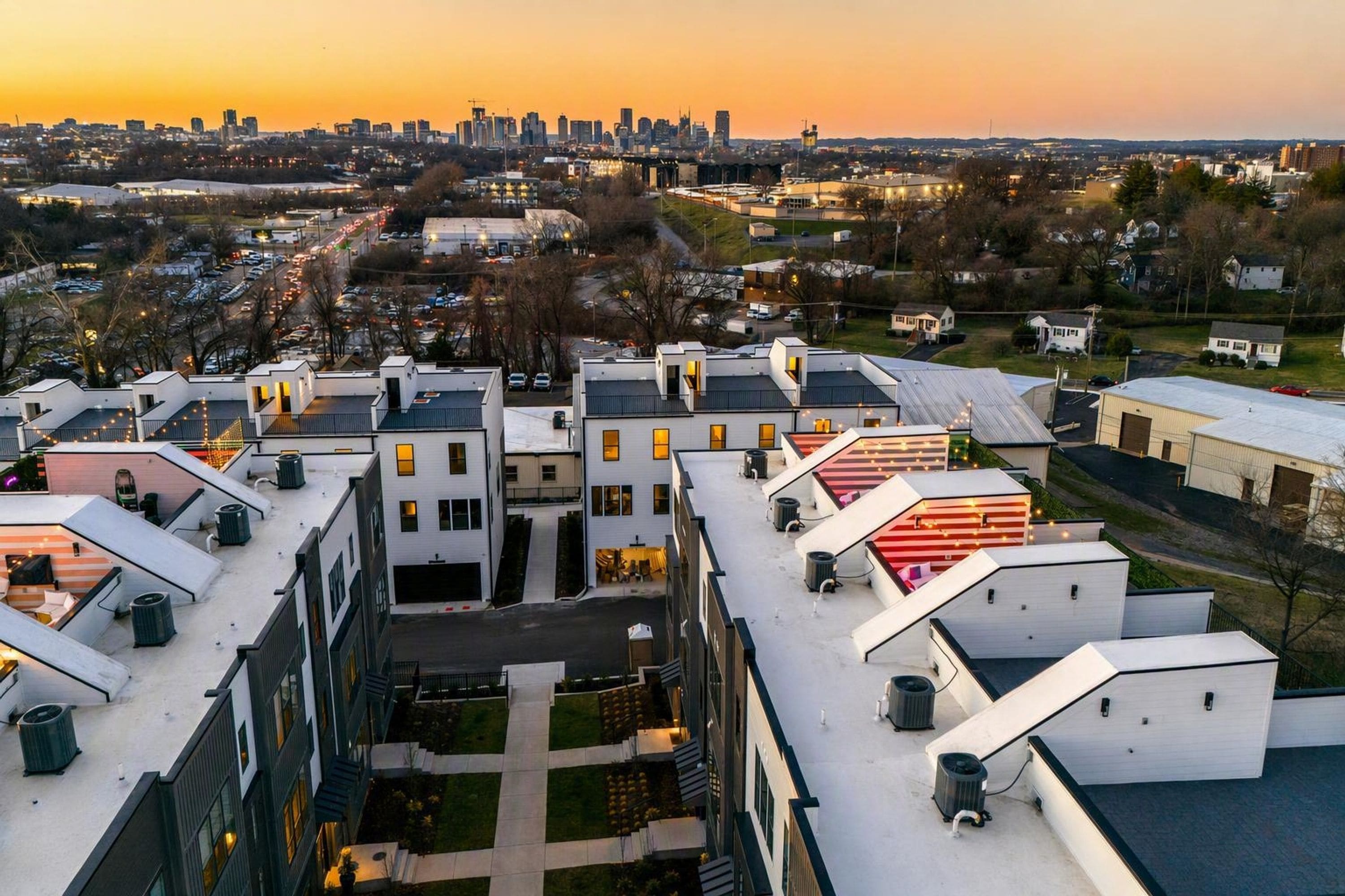 A modern apartment complex with multiple buildings, rooftop terraces, and a city skyline in the background.