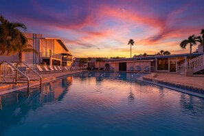 A swimming pool with a sunset view, a building with a balcony, and palm trees. - Walk to Beach Heated Pool - Madeira Beach 2BR (Madeira Beach)