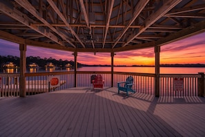 A wooden deck with a view of a sunset over water, two Adirondack chairs, and a railing. - 12 Floors Up With King Bunks and Resort Pool (Orlando)
