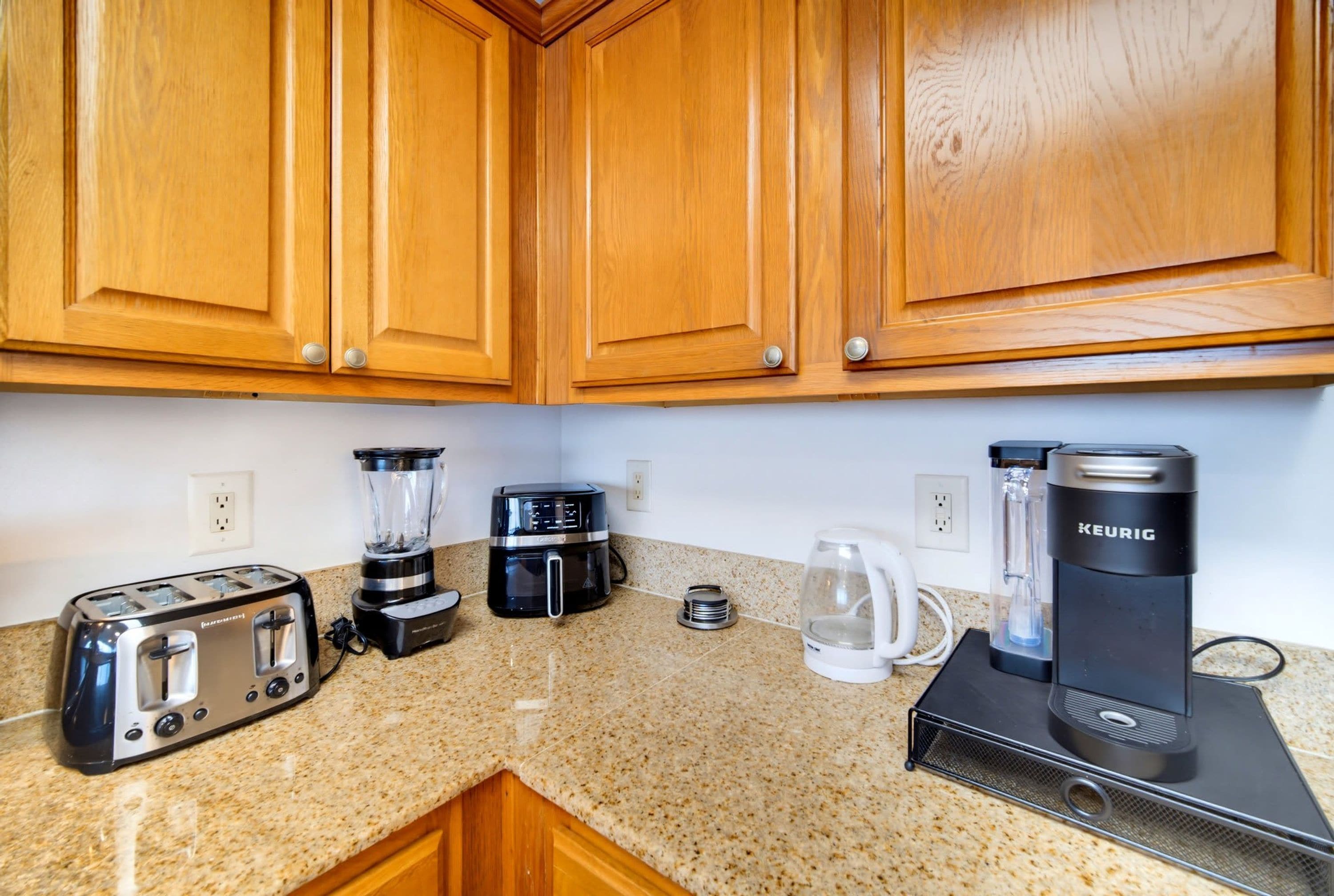 A kitchen with wooden cabinets, a toaster, a blender, a coffee maker, and a kettle.