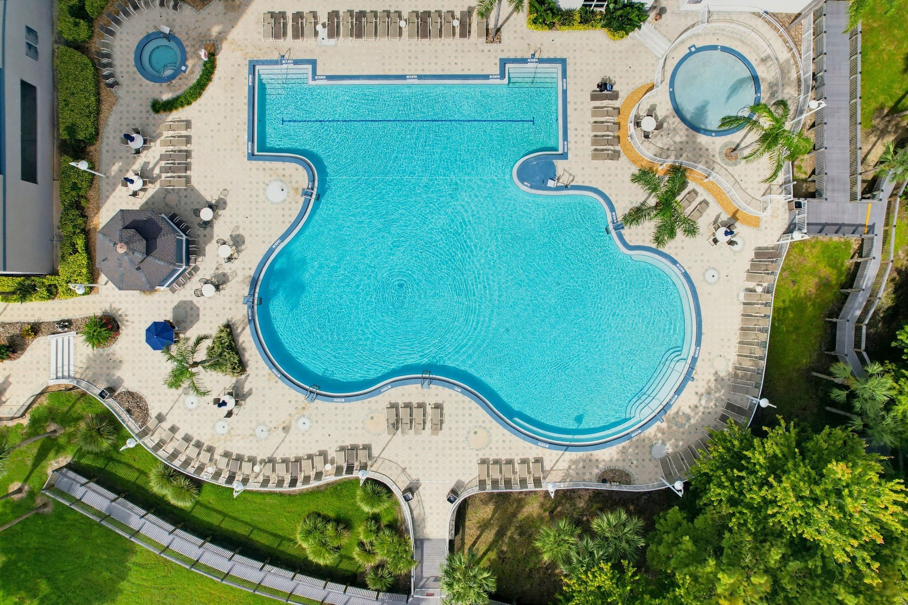 A large swimming pool with a unique shape, surrounded by sun loungers and a small circular pool.
