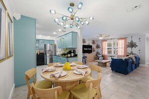 Ein modernes Wohnzimmer mit einem blauen Sofa, einem Esstisch für vier Personen und einer Küche im Hintergrund.