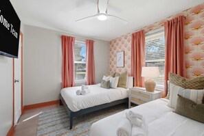 Ein Hotelzimmer mit zwei Betten, einem Flachbildfernseher, einem Deckenventilator und einem Fenster mit Jalousien.