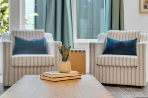 A room with two striped armchairs, a small table with a plant and books, and a window with curtains. - Nashville Hideaway Private Rooftop City View (Nashville)