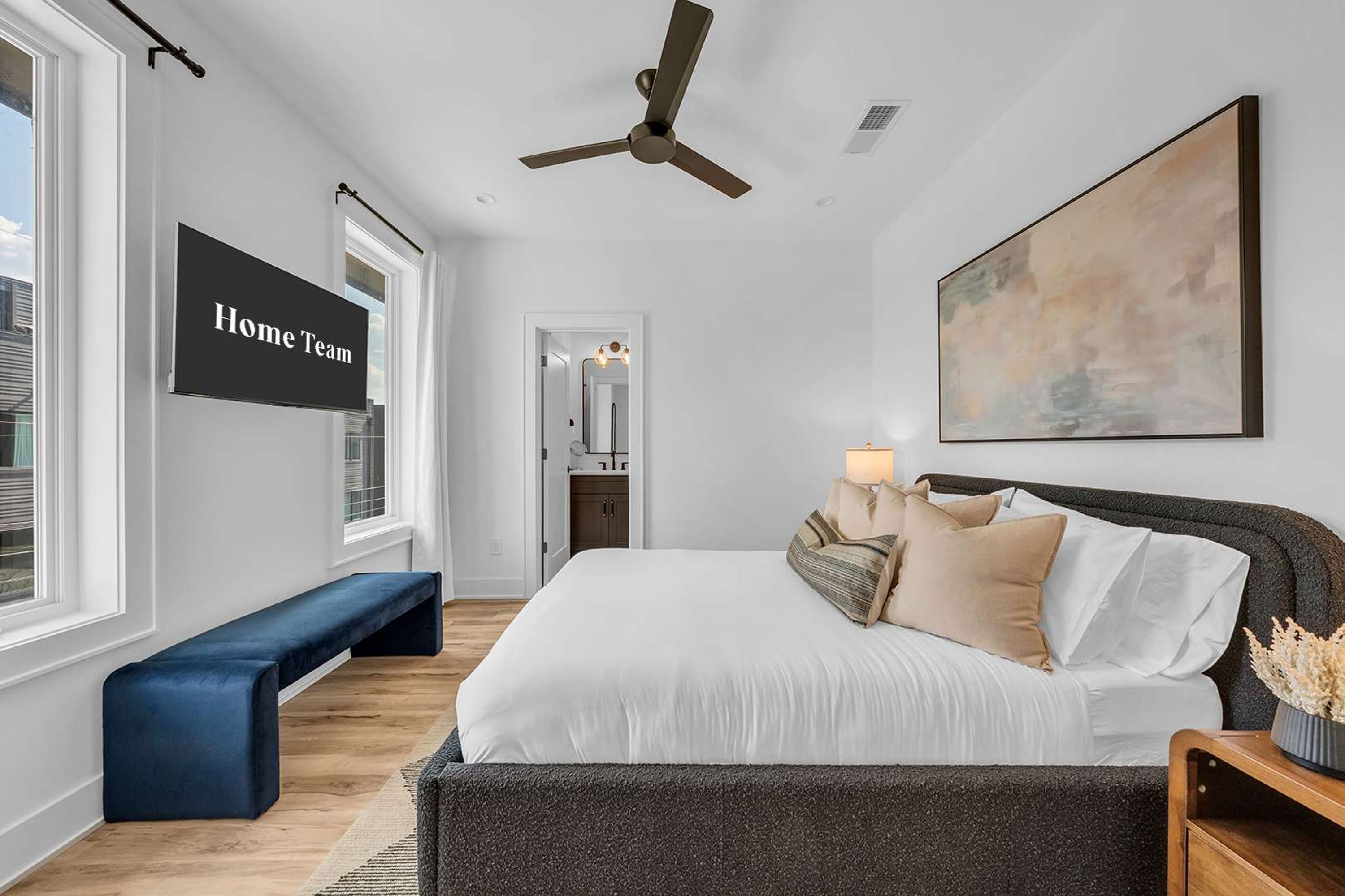 A bedroom with a bed, a bench, a ceiling fan, a TV, and a painting.