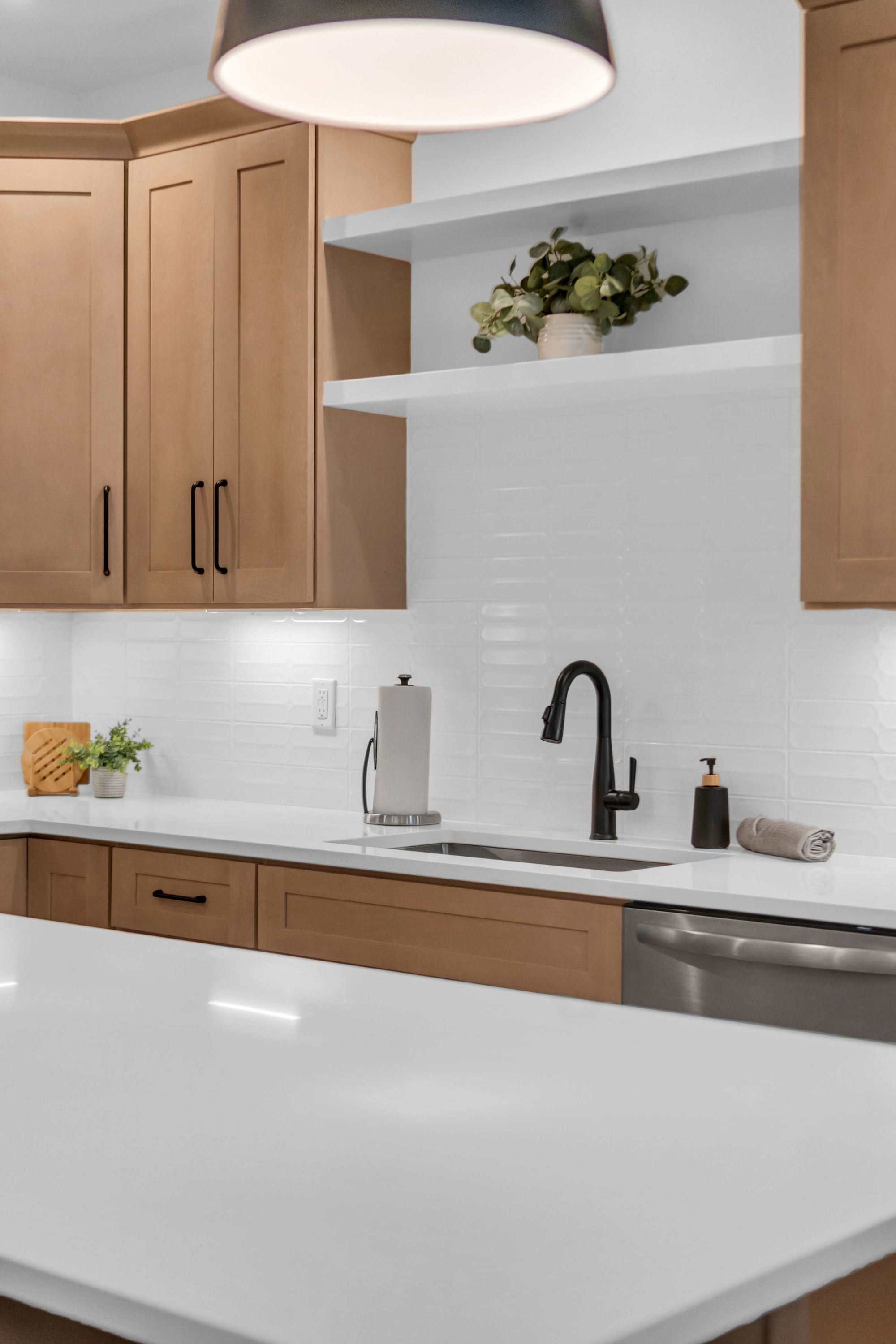 A modern kitchen with wooden cabinets, a white countertop, a black faucet, and a hanging light fixture.