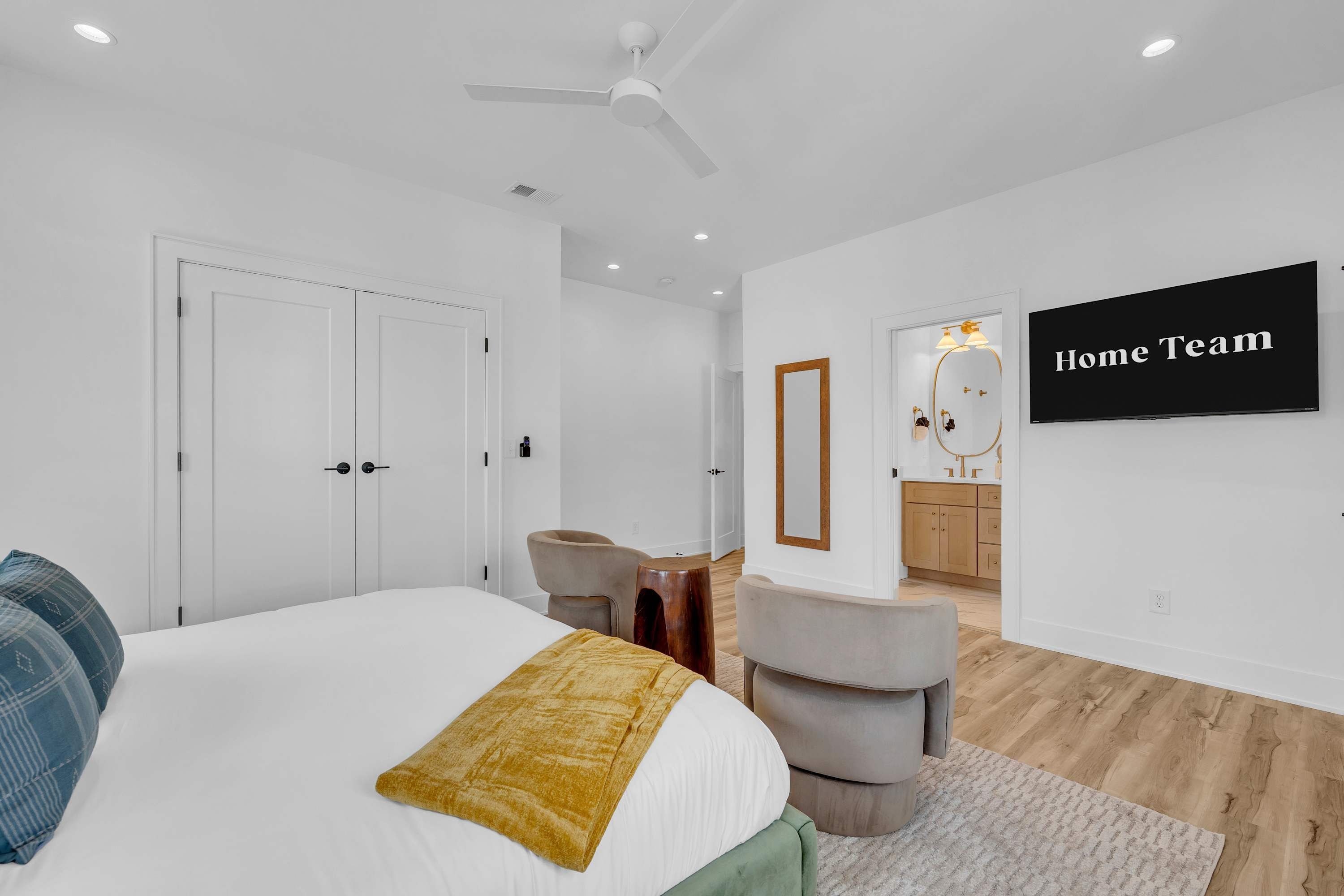 A modern bedroom with a bed, a ceiling fan, a TV, and a bathroom visible through an open door.