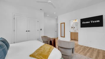A modern bedroom with a bed, a ceiling fan, a TV, and a bathroom visible through an open door.