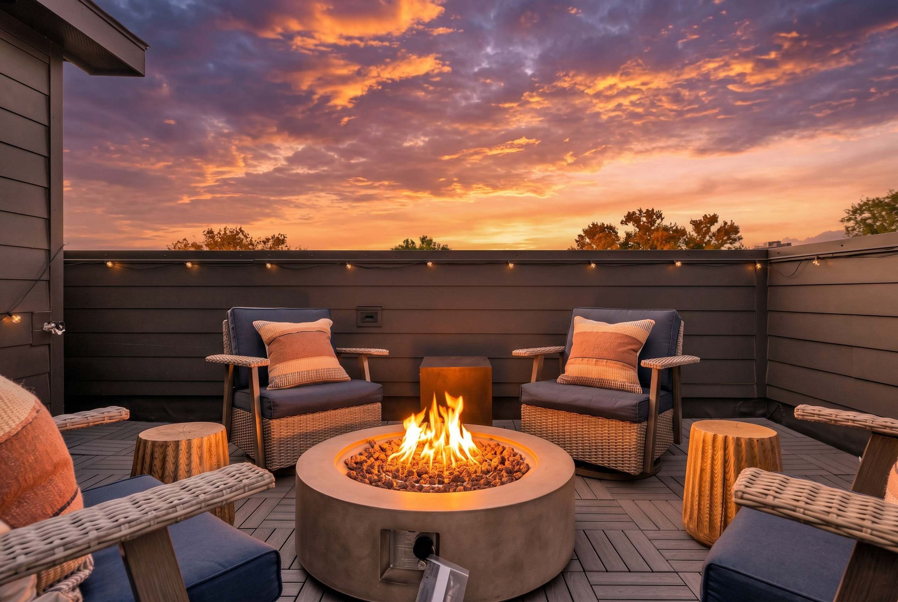 A rooftop patio with a fire pit, wicker furniture, and a view of the sunset.