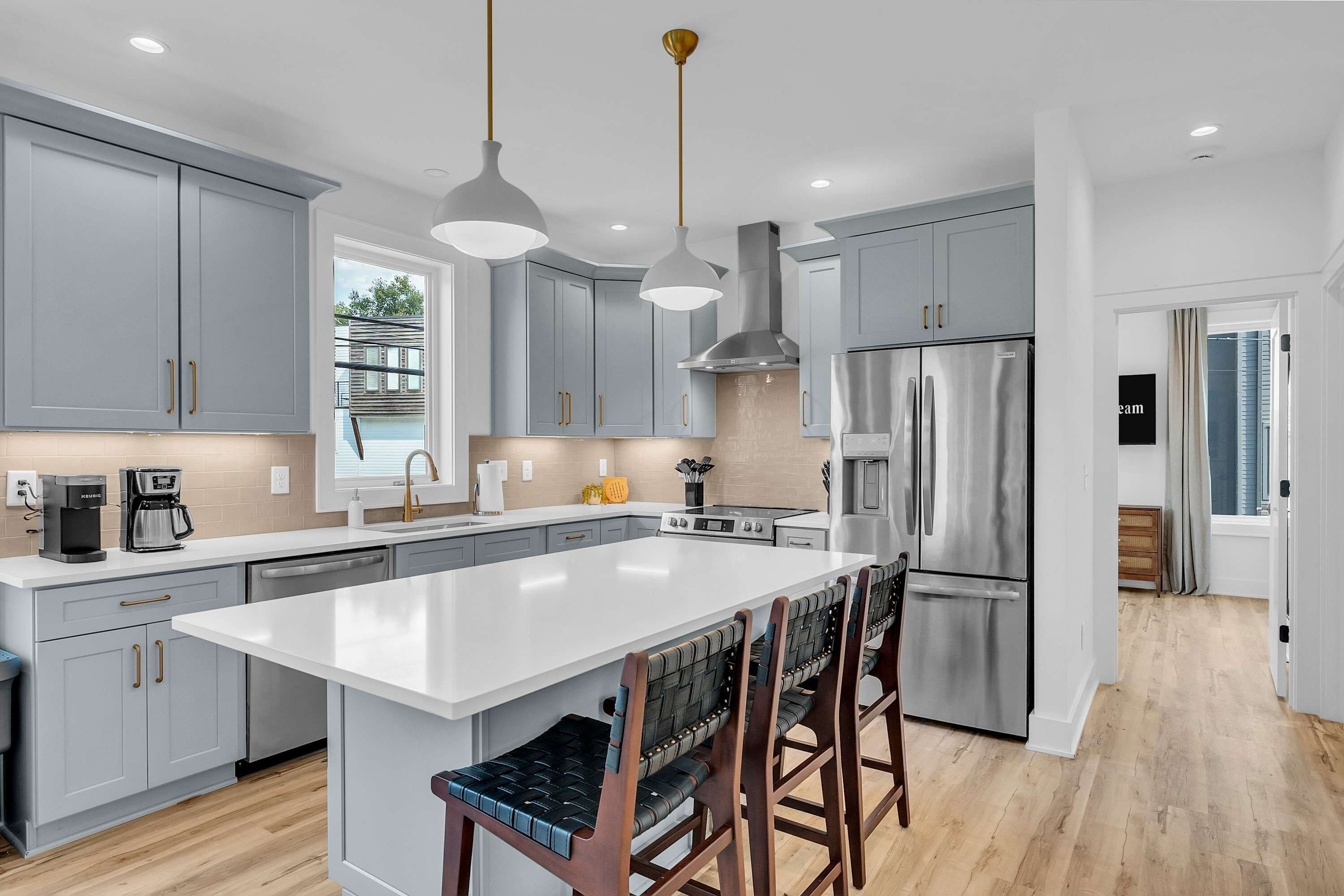 A modern kitchen with grey cabinets, a stainless steel refrigerator, and a central island with bar stools.