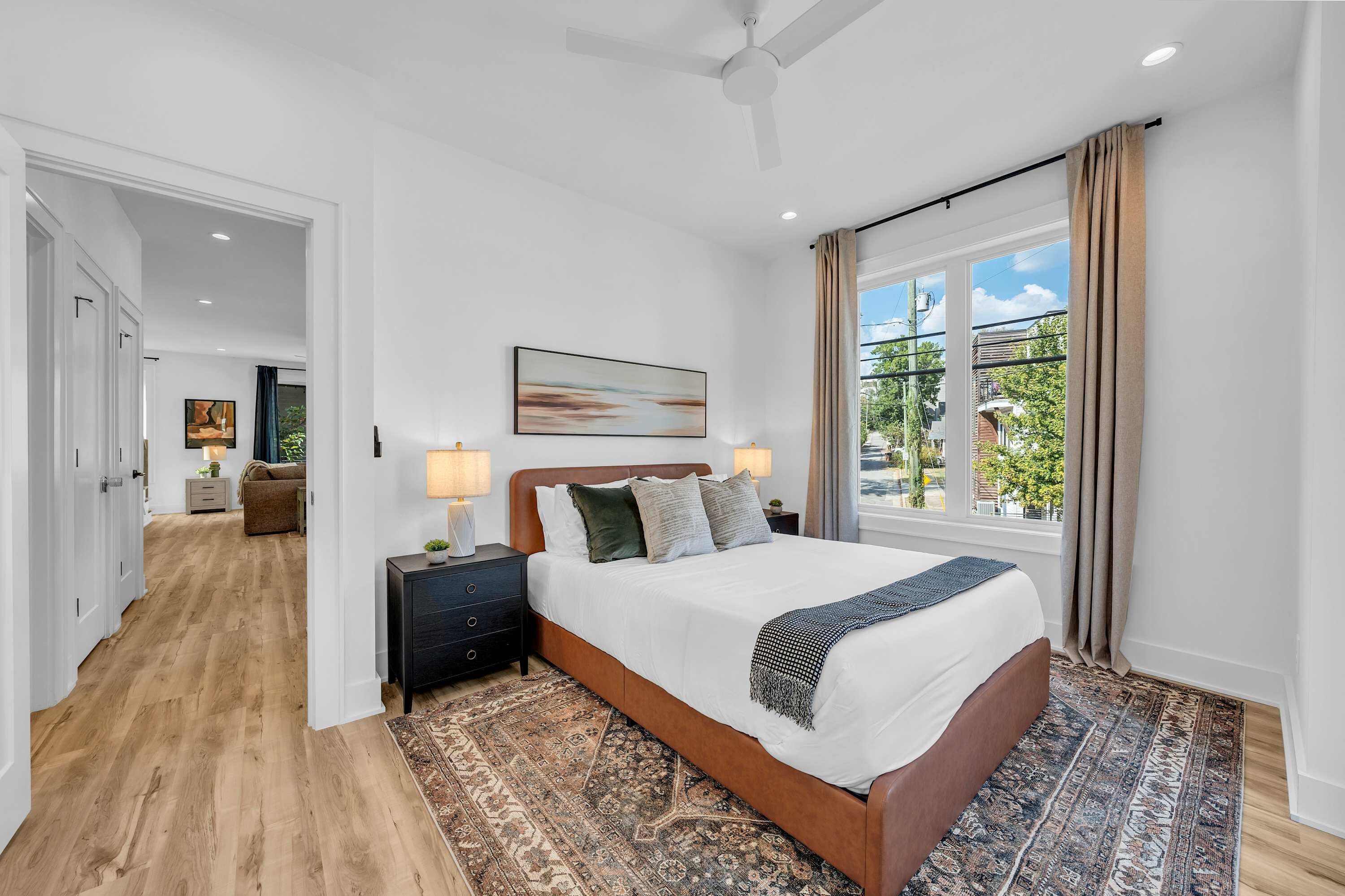 A hotel room with a large bed, a nightstand, a lamp, a painting, and a view of the outdoors.