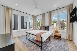 Quarto moderno com cama, mesa de cabeceira, abajur e televisão.