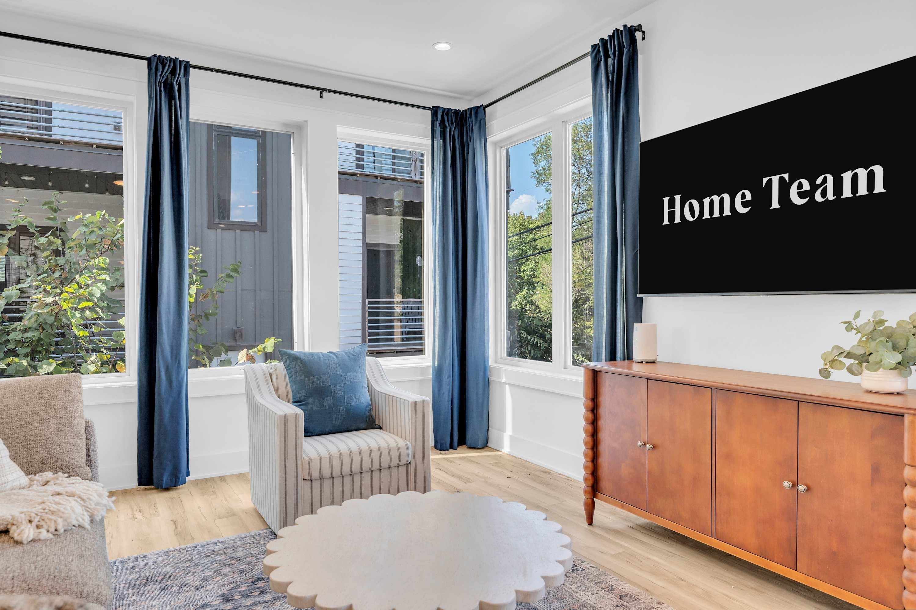 A modern living room with a large flat-screen TV, a striped armchair, a round coffee table, and a wooden cabinet.