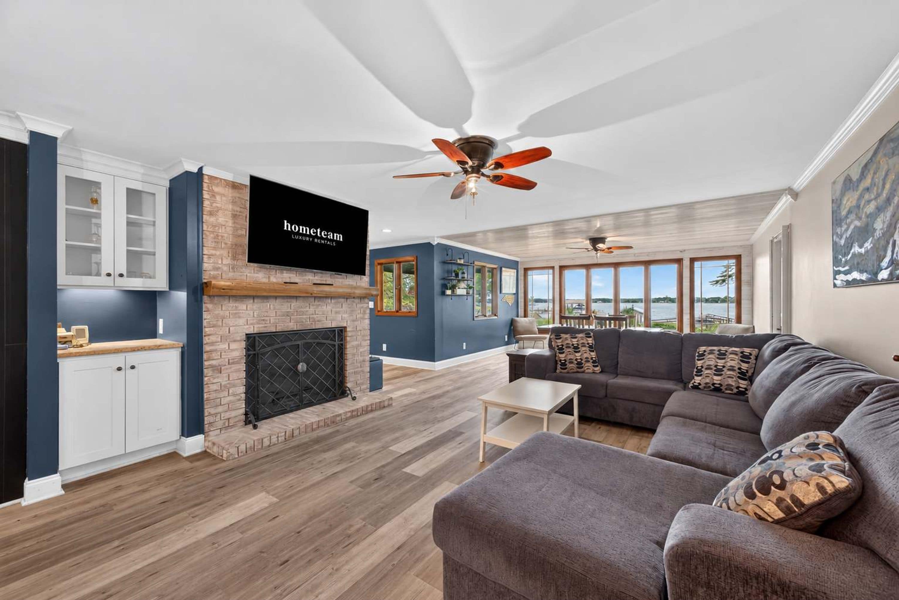 A modern living room with a fireplace, a television mounted on the wall, and a large window offering a view of the outdoors.