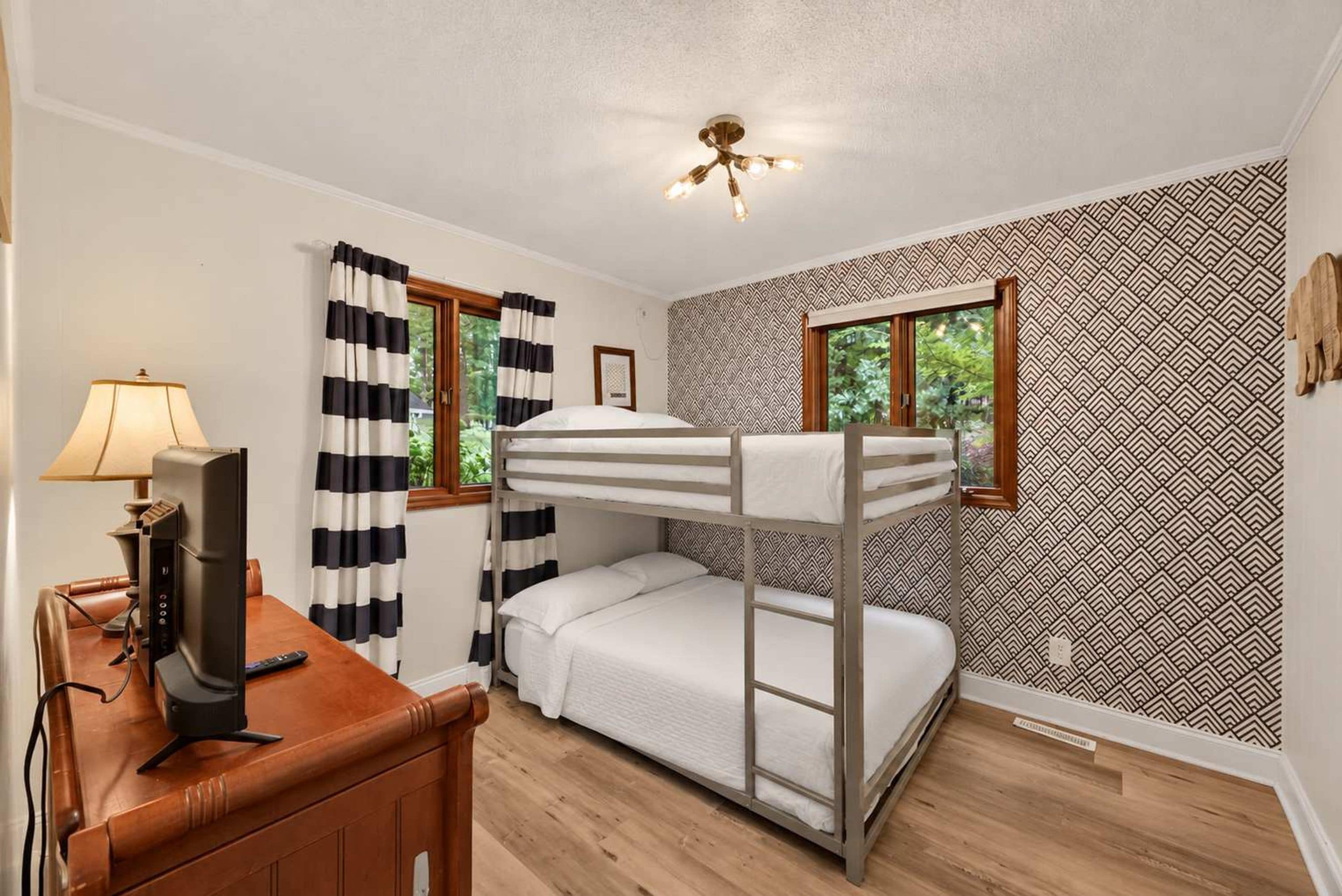A bunk bed room with a desk, lamp, and patterned wallpaper.