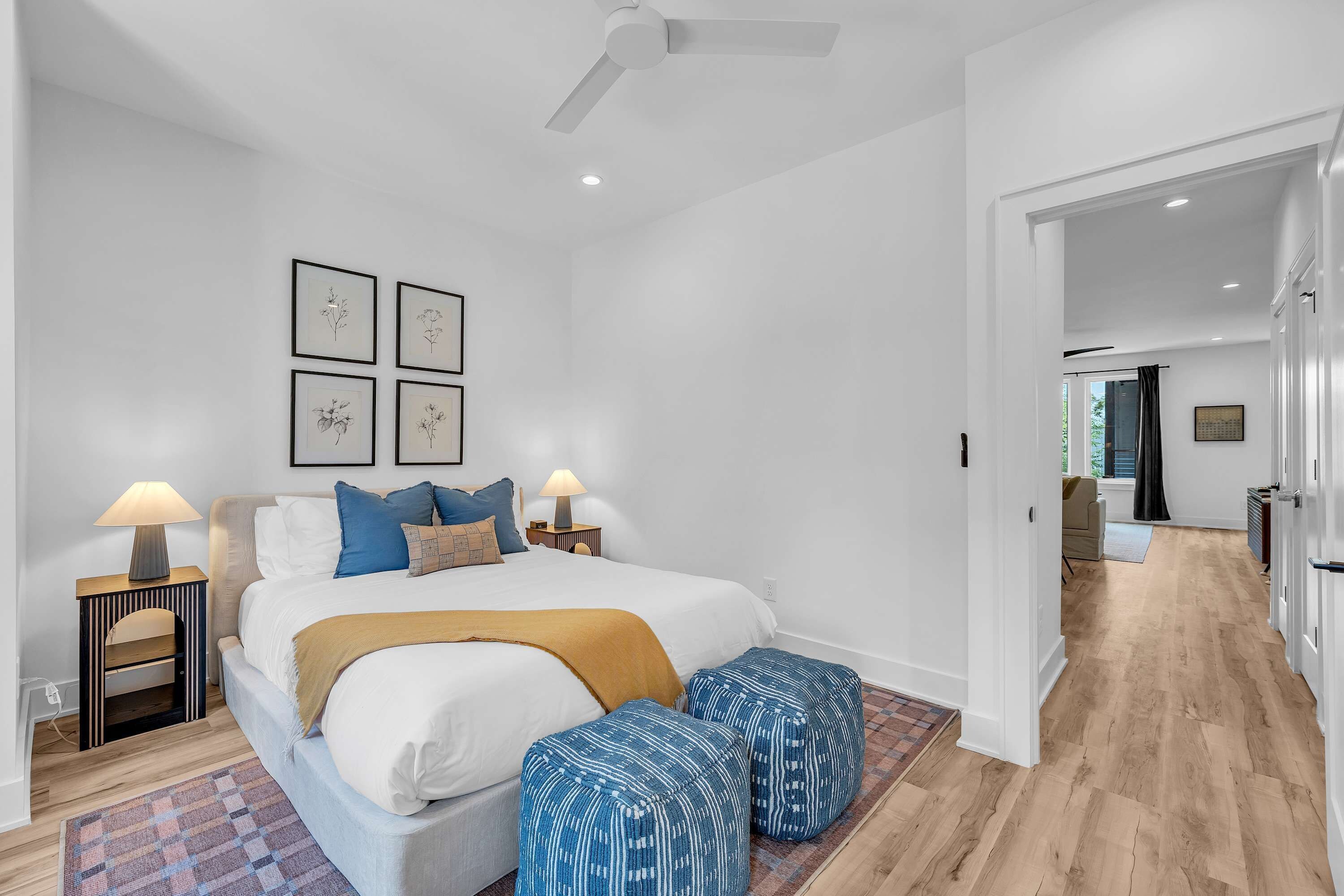Une chambre à coucher comprenant un lit, des tables de chevet, des lampes, un ventilateur de plafond et des reproductions encadrées de motifs botaniques accrochées au mur.