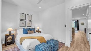 Une chambre à coucher comprenant un lit, des tables de chevet, des lampes, un ventilateur de plafond et des reproductions encadrées de motifs botaniques accrochées au mur.