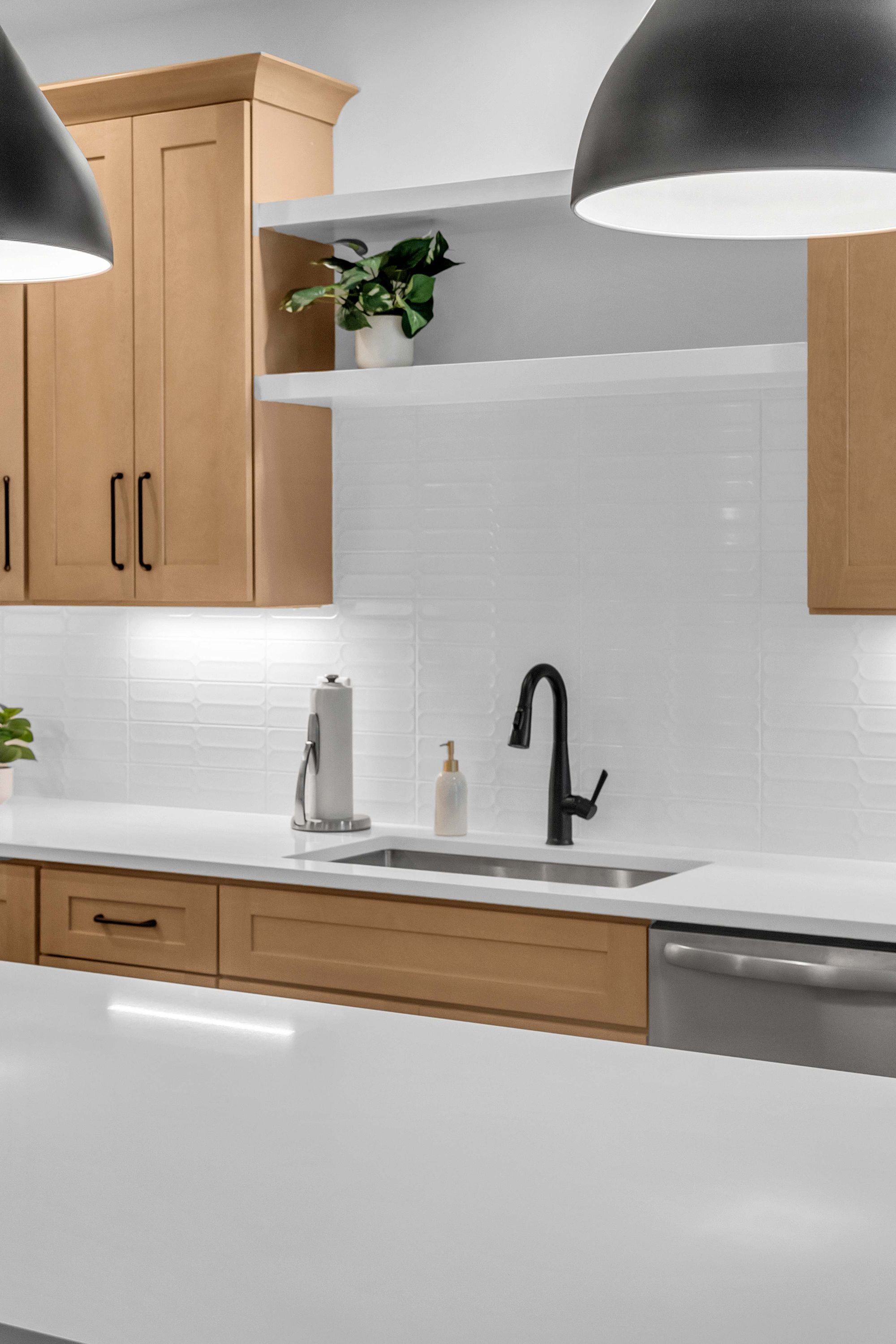 Une cuisine moderne avec des meubles en bois, un plan de travail blanc, un robinet noir et une plante en pot.