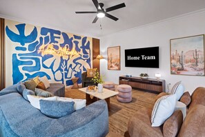 A modern living room with a ceiling fan, a large abstract painting, a flat-screen TV, and a sofa set. - Adobe Afterglow Swim Soak Play Stay Awhile (Mesa)
