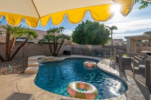 A swimming pool with a curved edge, surrounded by a stone wall, palm trees, and a yellow umbrella. - Adobe Afterglow Swim Soak Play Stay Awhile (Mesa)