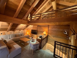 A cozy loft bedroom with a wooden ceiling, a sofa, a TV, and a lamp. - Chalet 'Le Manoir Valloire Ski' (Valloire)