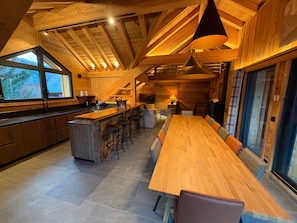 A modern kitchen with a central island, bar stools, and a long dining table. - Chalet 'Le Manoir Valloire Ski' (Valloire)
