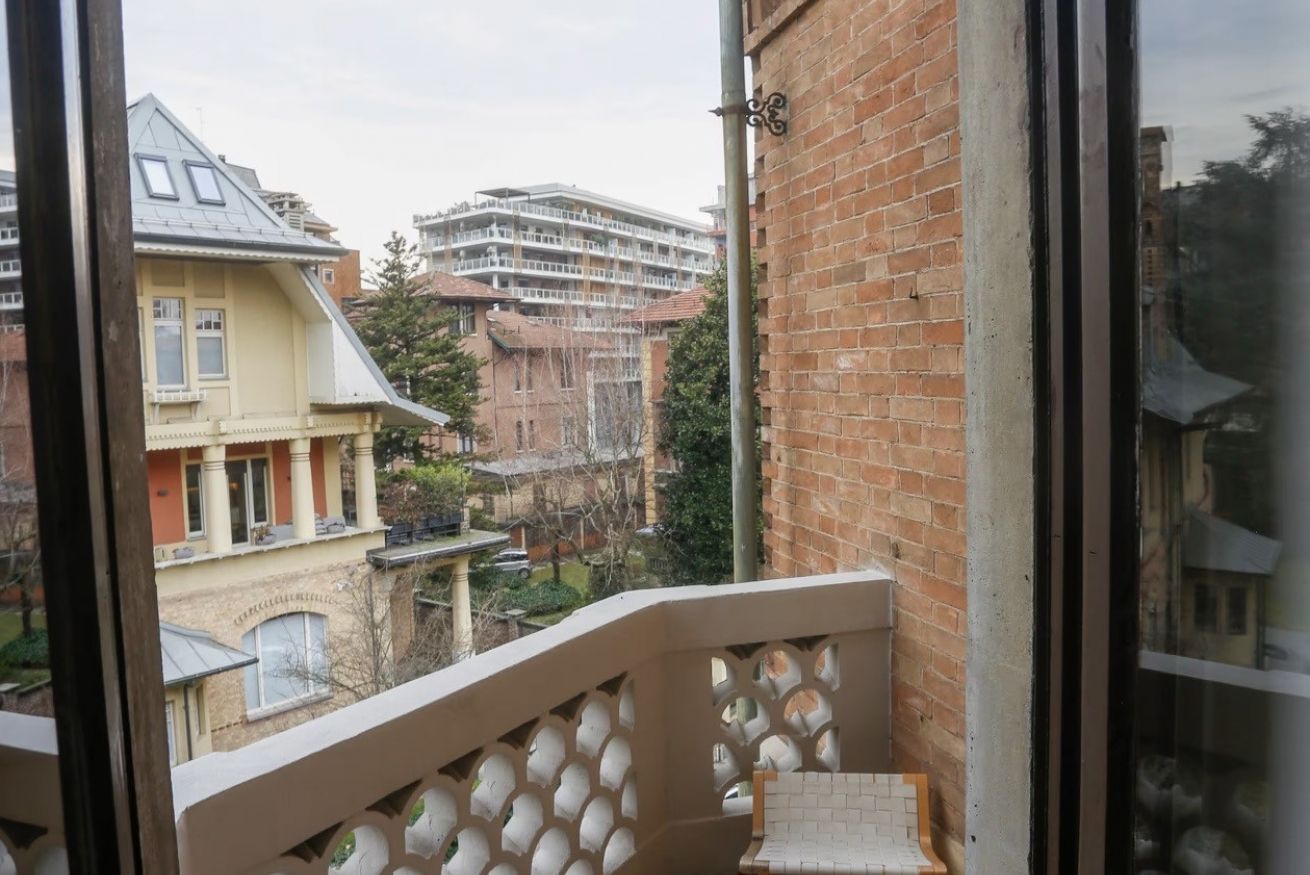 Ein Balkon mit Blick auf umliegende Gebäude, darunter ein mehrstöckiges Haus mit Balkonen.